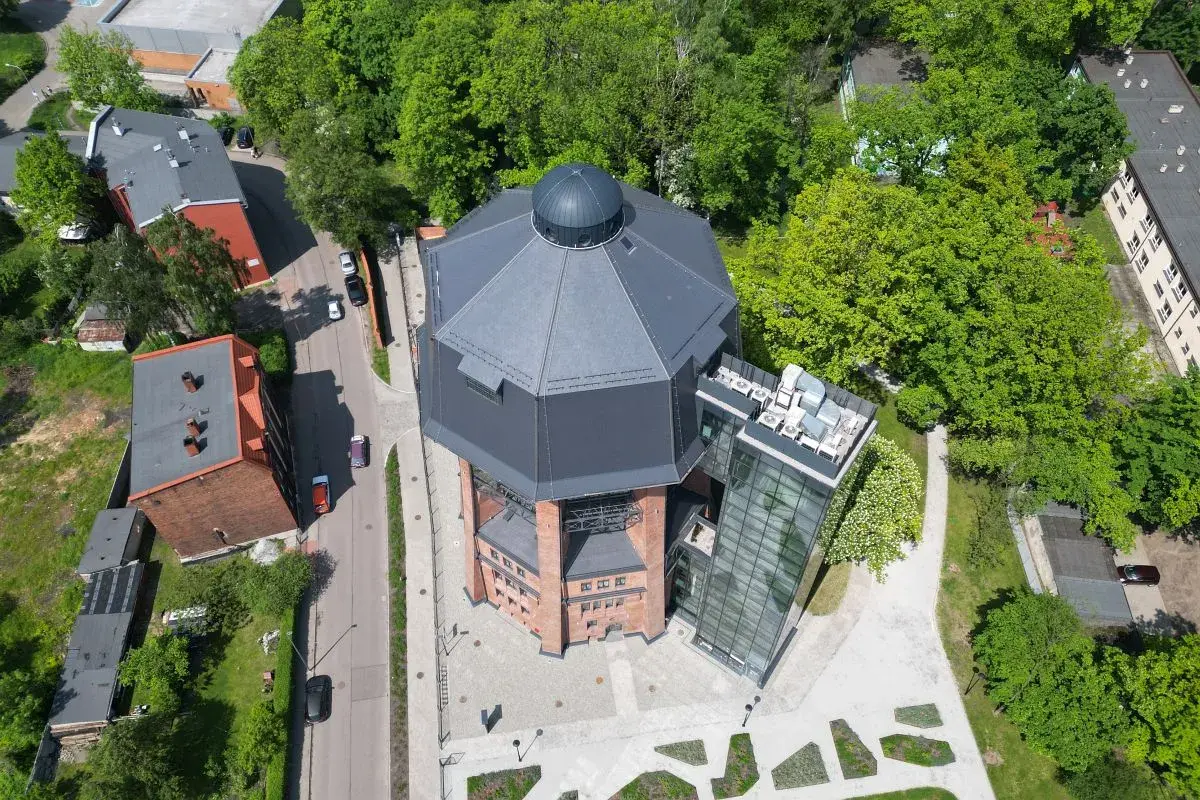 Nowoczesna wieża ciśnień w Zabrzu z przeszkloną windą i tarasem widokowym, otoczona zielenią.
