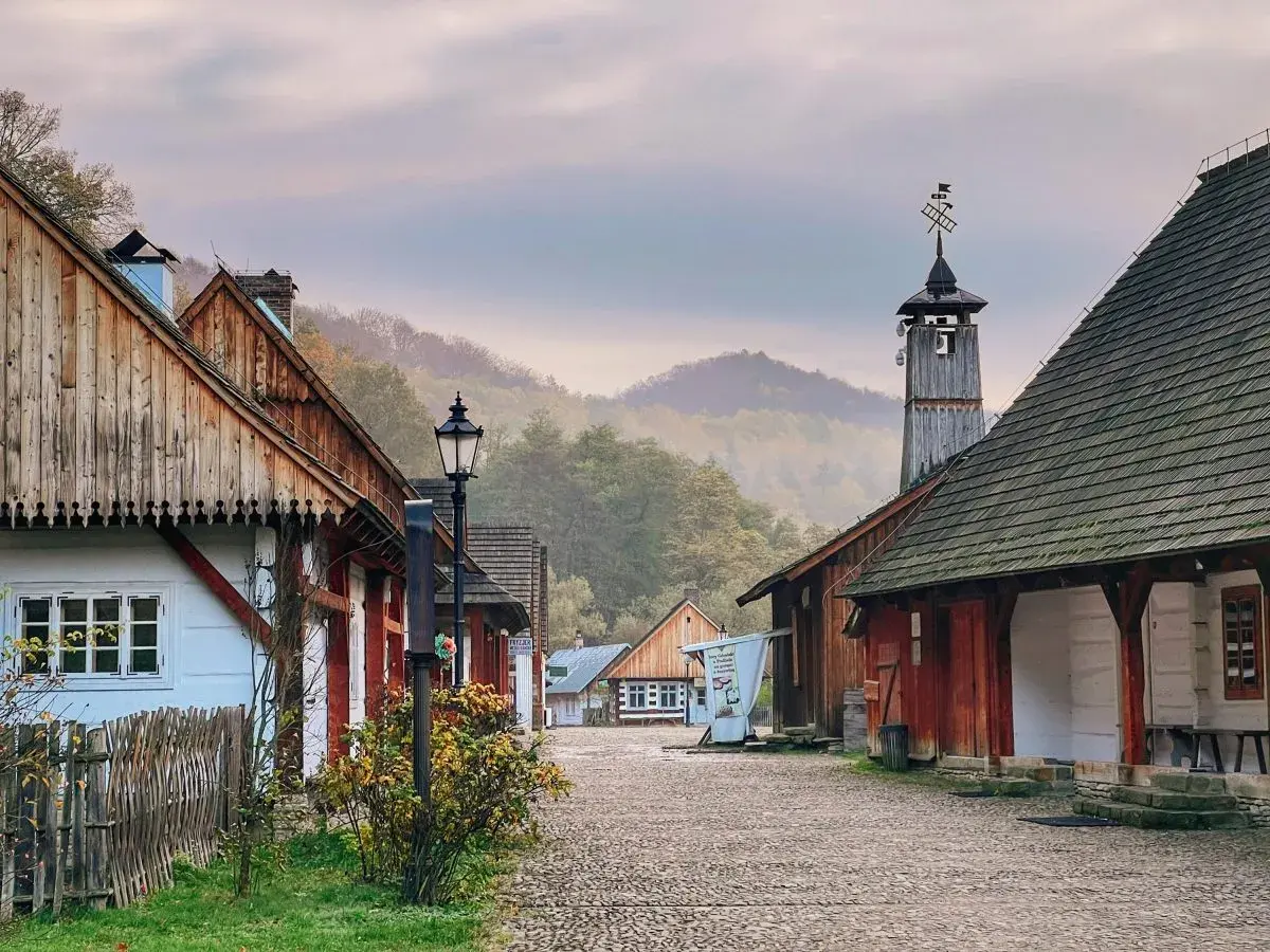 Sanok atrakcje: skansen z drewnianymi domami i wieżą, otoczony mglistymi wzgórzami.