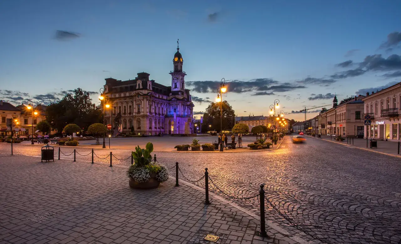 Wieczorny rynek w Nowym Sączu, oświetlony latarniami i iluminacją ratusza. Brukowana nawierzchnia i zabytkowa architektura tworzą niepowtarzalny klimat, zachęcając do odkrywania atrakcji Nowego Sącza.