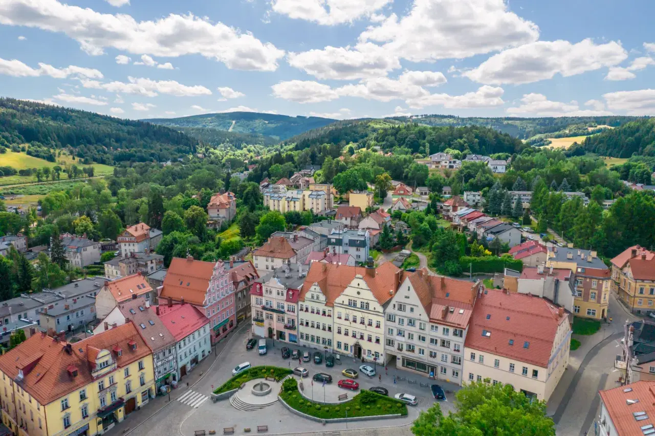 Urokliwy rynek i kolorowe kamienice w Dusznikach Zdroju. W tle zielone wzgórza, idealne na piesze wycieczki i odkrywanie atrakcji.