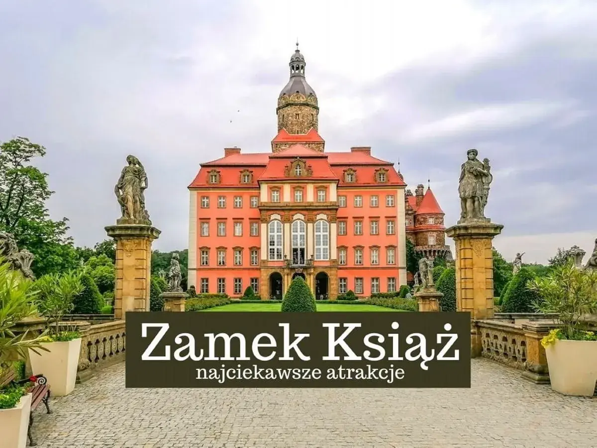Zamek Książ w Wałbrzychu, imponująca budowla z wieżą i rzeźbami, otoczona zielenią.