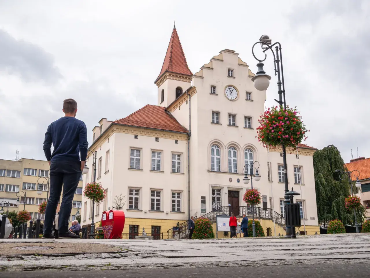 Mężczyzna podziwia ratusz w Trzebnicy, jedno z głównych atrakcji miasta. W tle zabytkowy budynek z zegarem i czerwonym dachem.