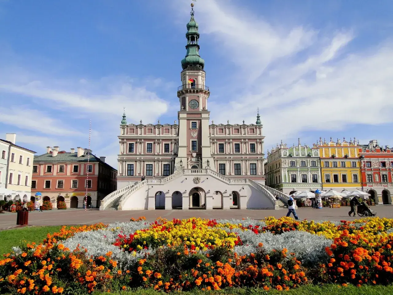 Zamość atrakcje: Ratusz i kolorowe kamienice na Rynku Wielkim, otoczone kwitnącymi rabatami.