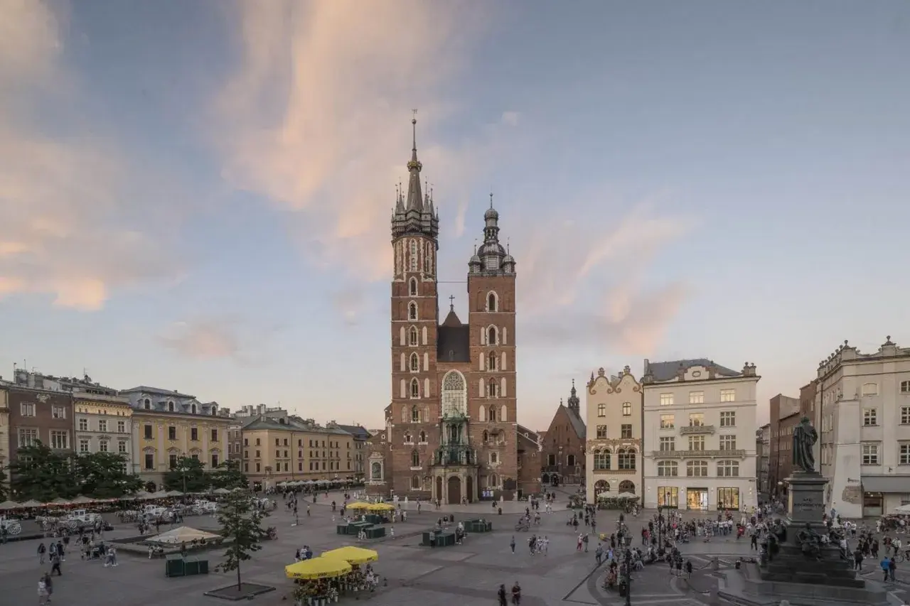 Majestatyczny kościół Mariacki na Rynku Głównym w Krakowie, otoczony kamienicami i placem tętniącym życiem.