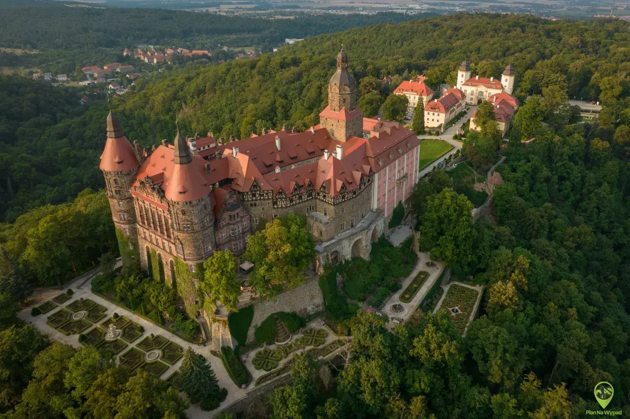 Zamek Książ otoczony lasami, z malowniczymi ogrodami i pobliską wsią. Rudawy Janowickie w tle.