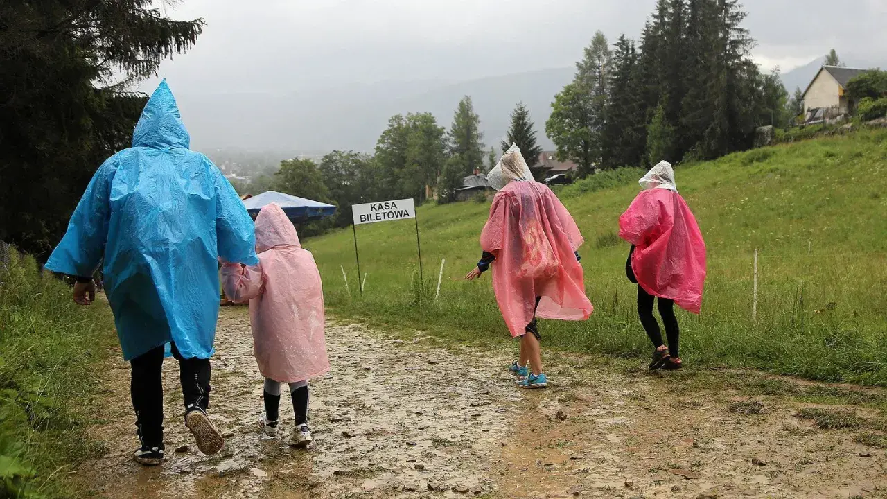 Rodzina w kolorowych pelerynach idzie błotnistą ścieżką. Nawet gdy pada deszcz, w Zakopanem można znaleźć ciekawe atrakcje.