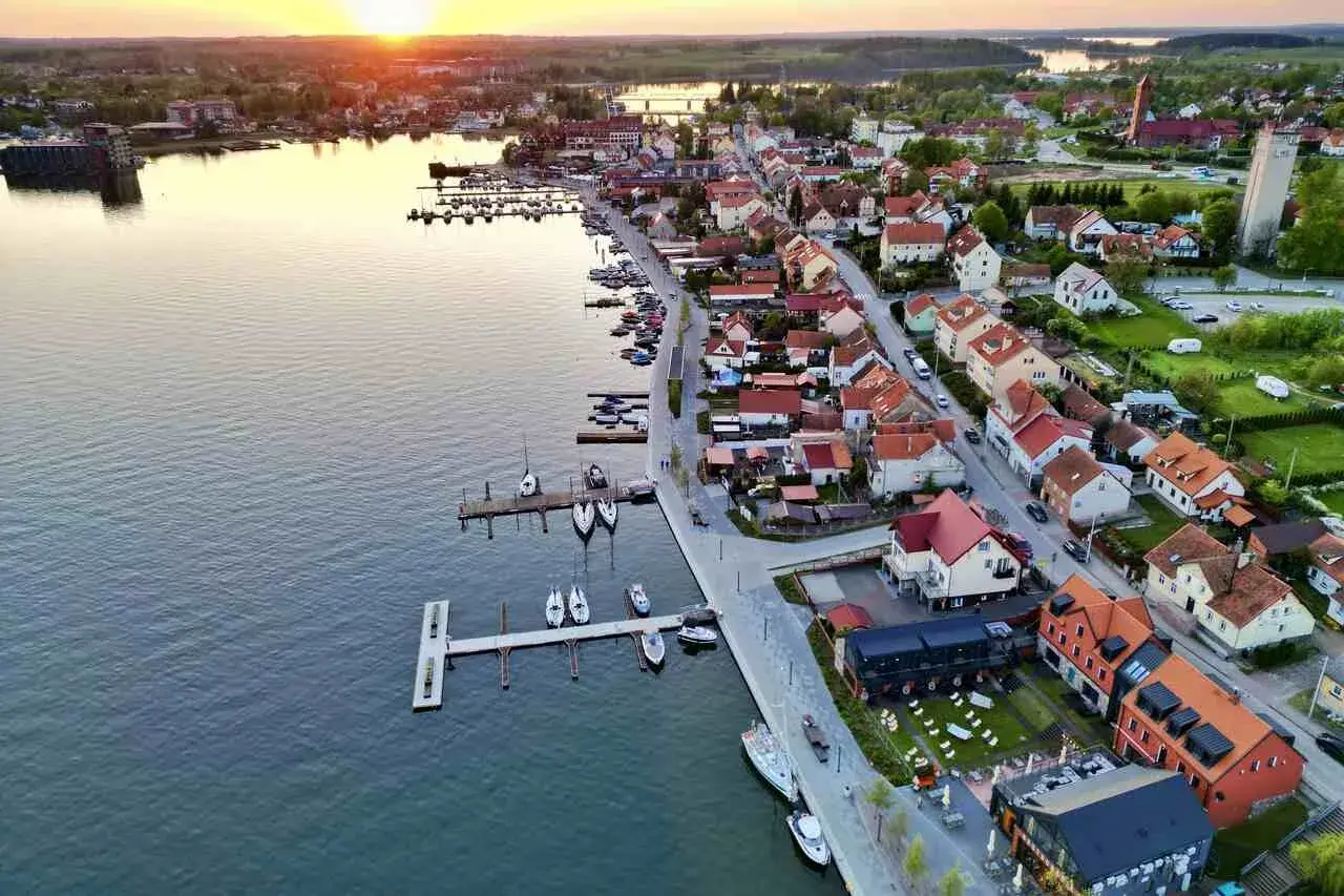 Zachód słońca nad jeziorem w Mikołajkach. Widok na port z łodziami i urokliwe miasteczko z czerwonymi dachami. Idealne miejsce na wakacyjne mikołajki atrakcje.