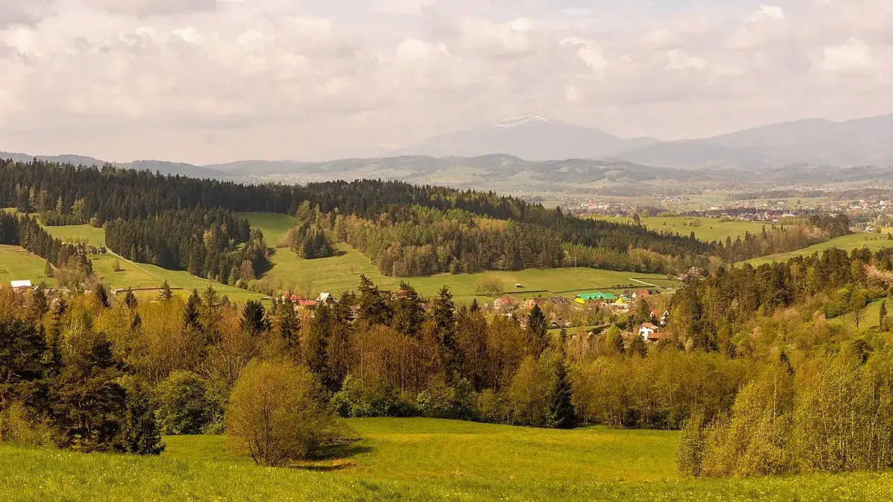 Malowniczy krajobraz z lasami i polami, w oddali widać góry i zabudowania. To idealne miejsce na odkrywanie rabka-zdrój atrakcje.