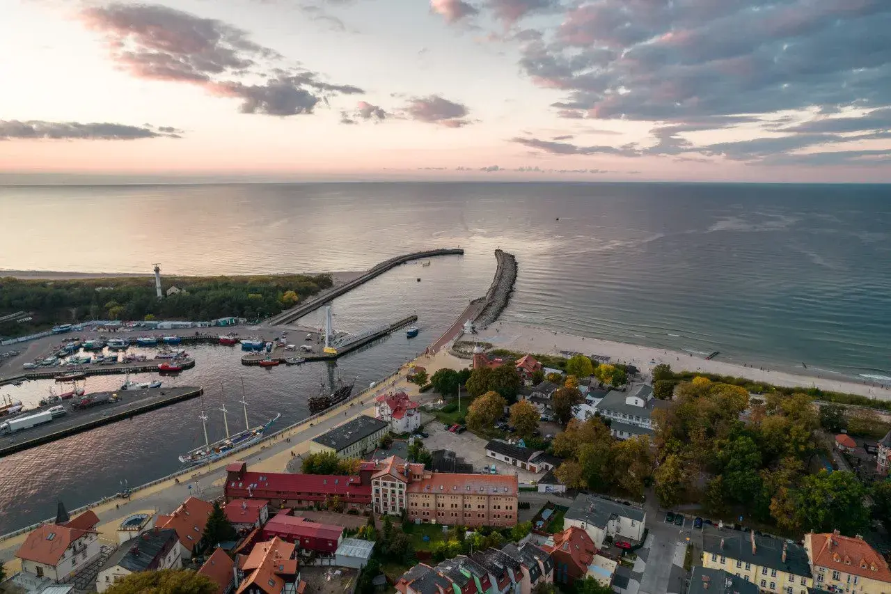 Widok na port i plażę w Ustce. Widać łodzie, latarnię morską i zabudowania. To jedne z wielu ustka atrakcje.