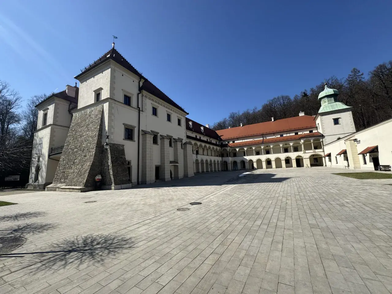 Zamek w Suchej Beskidzkiej, z dziedzińcem wyłożonym kamienną kostką i arkadowymi krużgankami, prezentuje się majestatycznie pod błękitnym niebem.