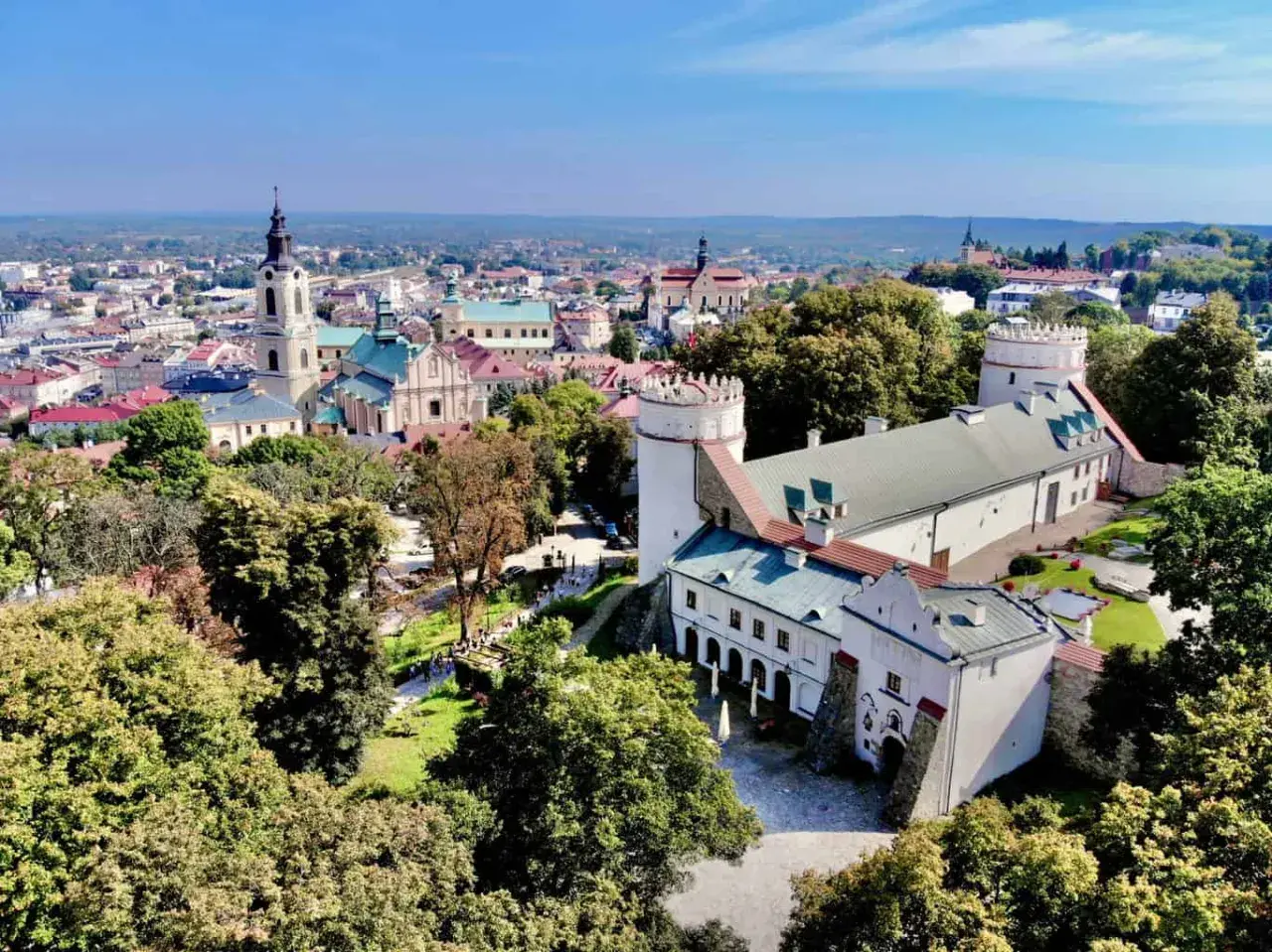Zamek w Sandomierzu i miasto z wieżą kościelną. Warto przemyśl atrakcje tego miejsca, spacerując po zielonych terenach.