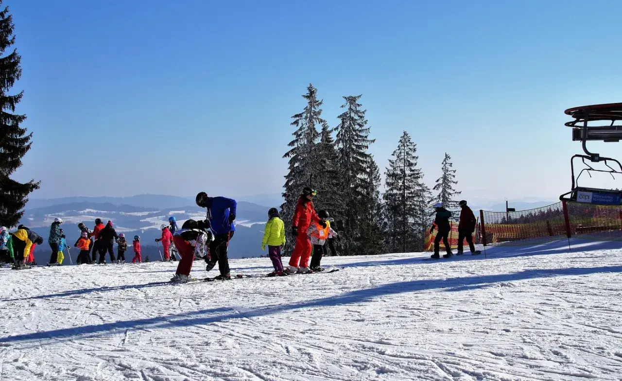 Słoneczny stok narciarski w Bieszczadach, z grupą narciarzy i snowboardzistów, w tym dzieci, przygotowujących się do zjazdu.