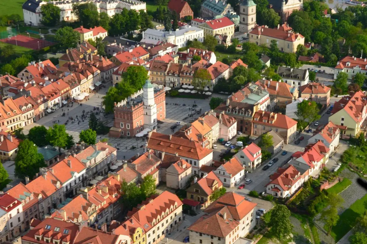 Urokliwe zabytkowe miasto nad Wisłą, z Rynkiem i wieżą ratuszową, otoczone kamienicami z czerwonymi dachami.