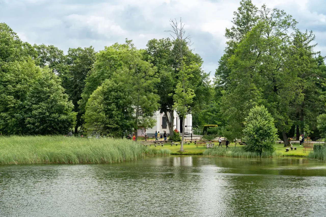 Malownicze jezioro i zielone tereny wokół białego budynku, idealne na spacer. Augustów atrakcje zachęcają do odpoczynku na łonie natury.
