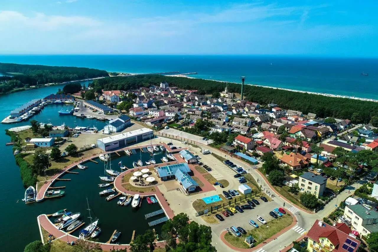 Widok z lotu ptaka na Dziwnów: port jachtowy, domy, las i morze. Wiele łodzi zacumowanych w marinie, idealne miejsce na wakacje.