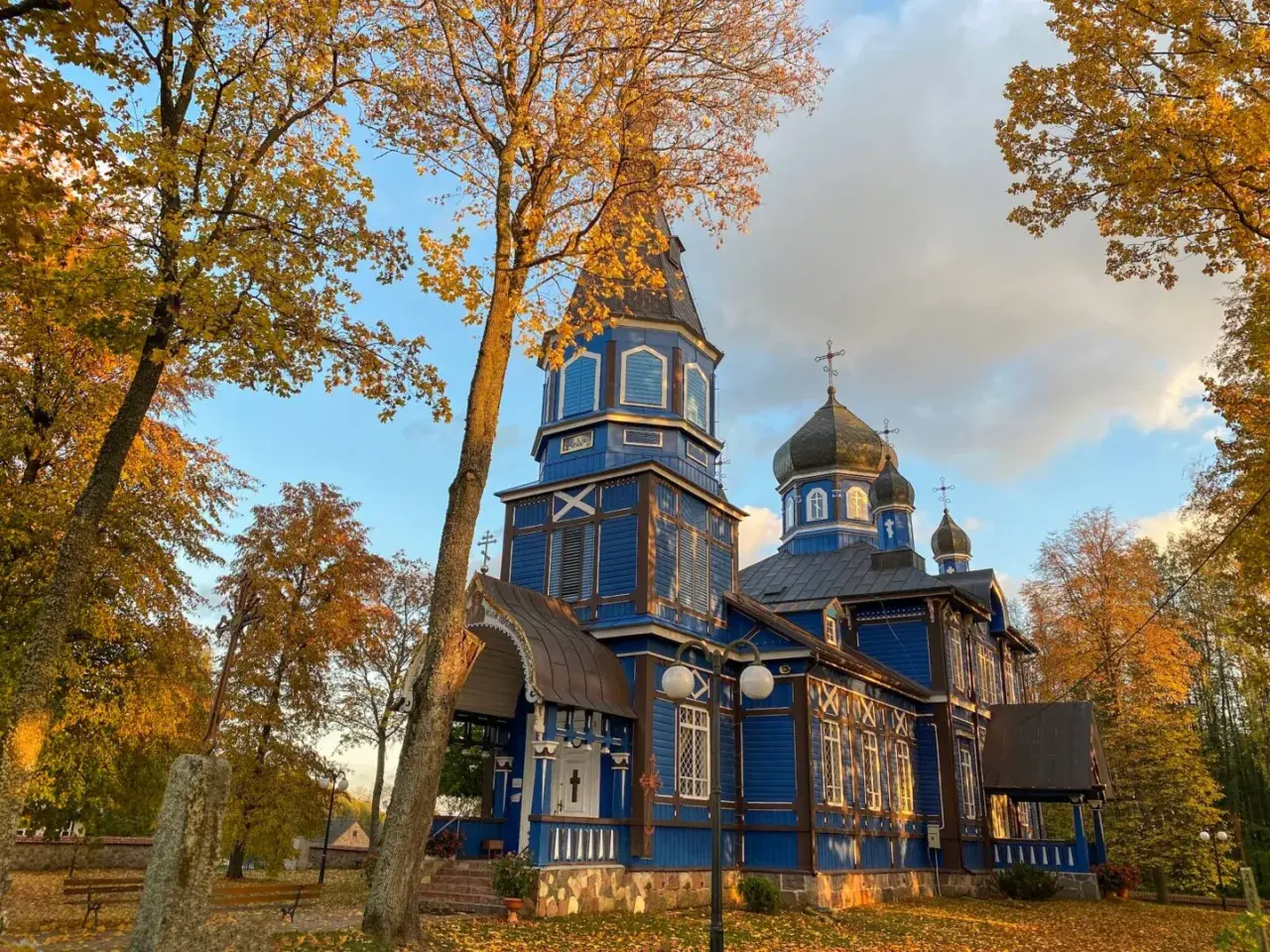 Jesienna odsłona cerkwi na Podlasiu. Złote liście i błękitne niebo podkreślają piękno drewnianej architektury, tworząc malownicze podlaskie atrakcje.