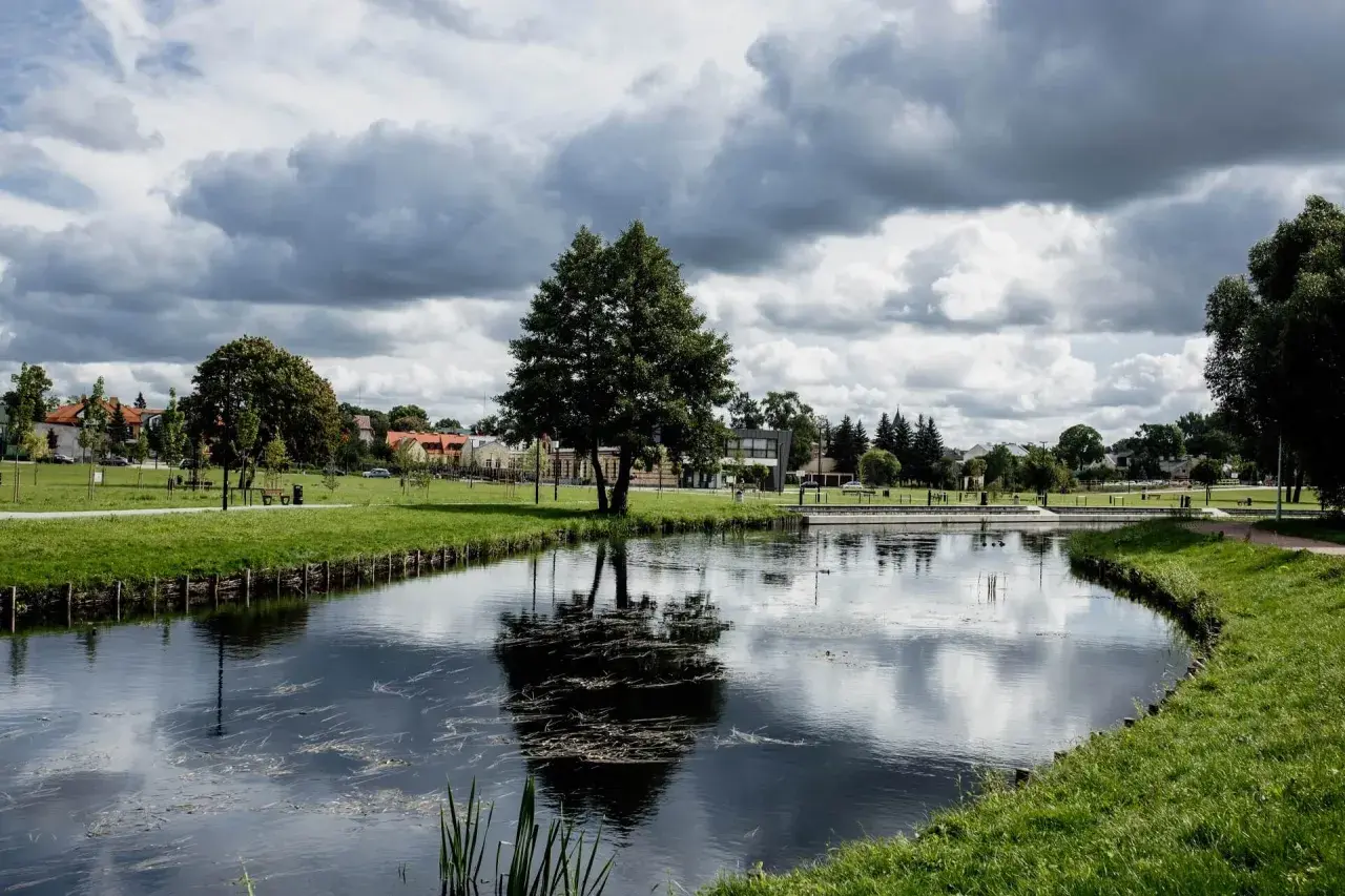 Spokojny park miejski w Suwałkach z jeziorem, drzewami i budynkami w tle. Idealne miejsce na relaks i odkrywanie suwalskich atrakcji.