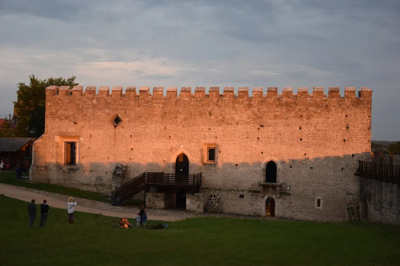 Zamek w Szydłowie o zachodzie słońca. Ludzie odpoczywają na trawie, podziwiając historyczne atrakcje.