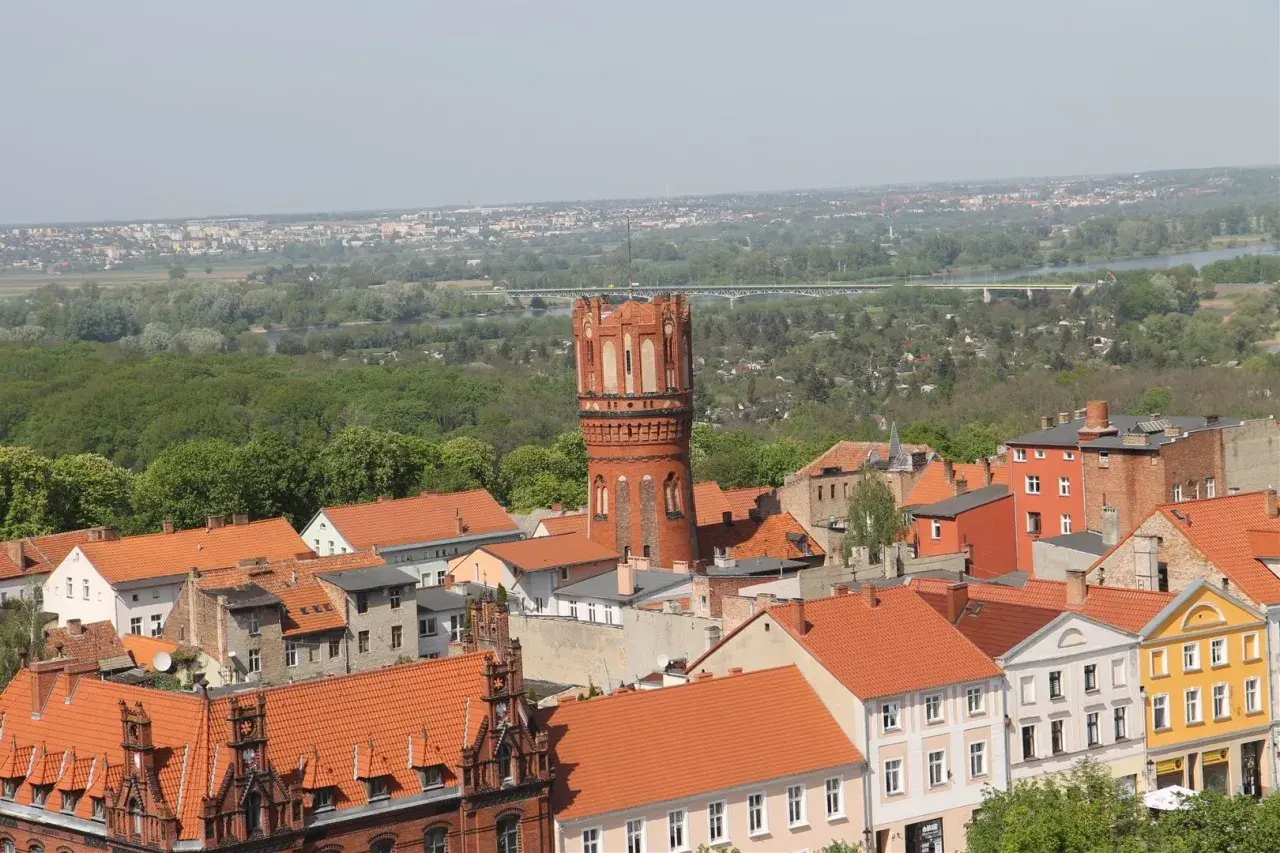 Widok na Chełmno z charakterystyczną wieżą ciśnień. Miasto z czerwonymi dachami i zielenią w tle. Chełmno atrakcje warte zobaczenia.