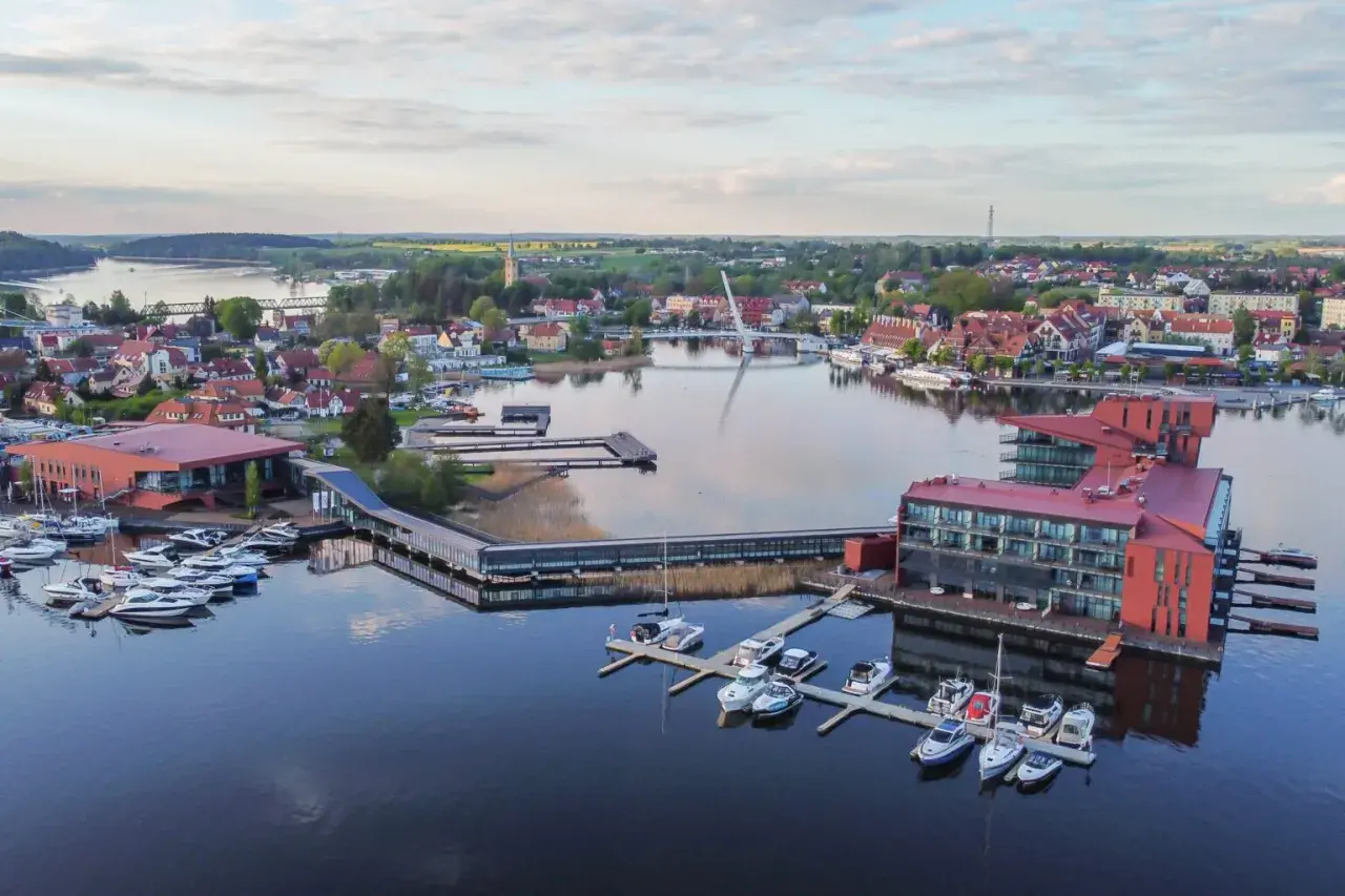Malownicze mazury miejscowości z nowoczesną architekturą nad jeziorem, pełne łodzi i jachtów.