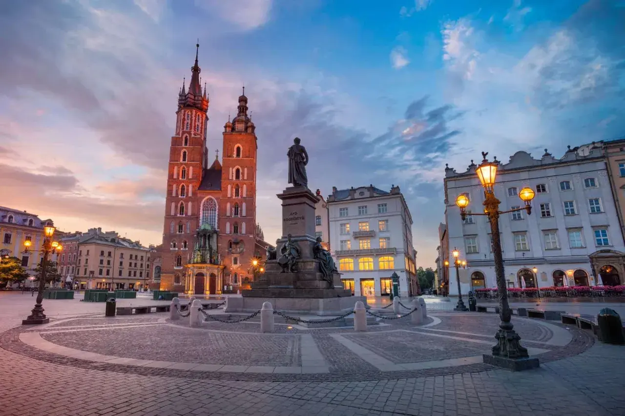 Kraków co zwiedzić? Rynek Główny z Kościołem Mariackim i pomnikiem Mickiewicza o zachodzie słońca. Idealne miejsce na spacer.
