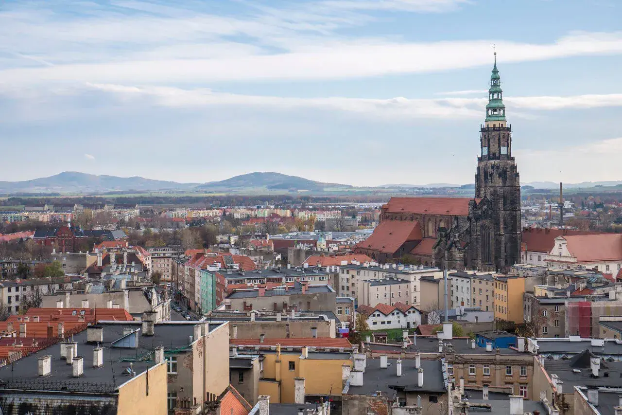Widok na miasto z dominującą wieżą kościoła. W oddali góry. **Świdnica atrakcje** zachwycają.