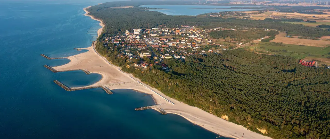 Jarosławiec atrakcje: malownicza plaża z falochronami, lasy sosnowe i zabudowania kurortu nad Bałtykiem.