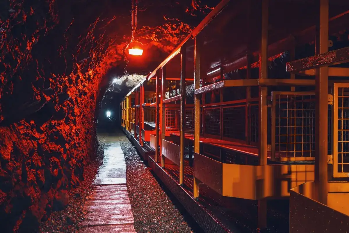 Wagoniki turystyczne w kopalni w Złotym Stoku czekają na pasażerów w mrocznym, oświetlonym na czerwono tunelu.