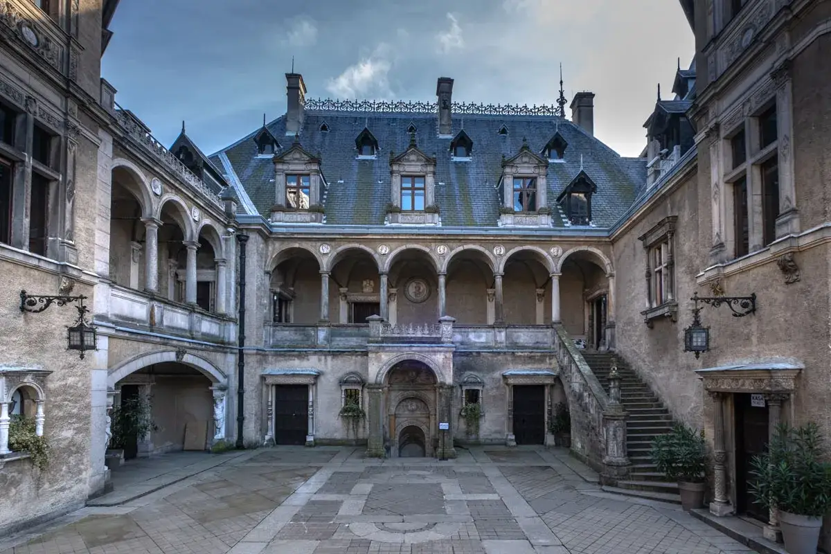 Dziedziniec zamku w Gołuchowie z arkadowymi krużgankami, kamiennymi schodami i zabytkową architekturą.