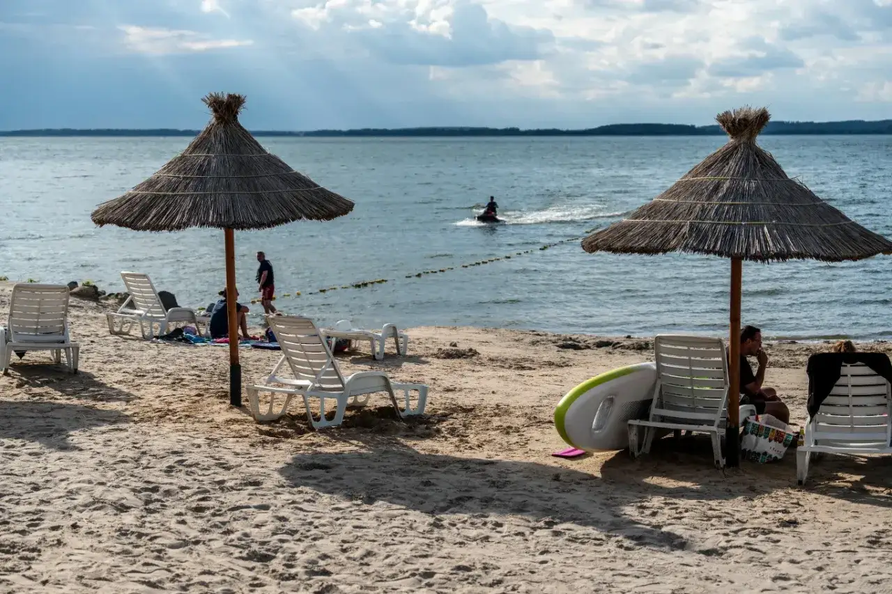 Słoneczny dzień nad polskim jeziorem. Leżaki, parasole i wodny skuter zapraszają na wakacje.