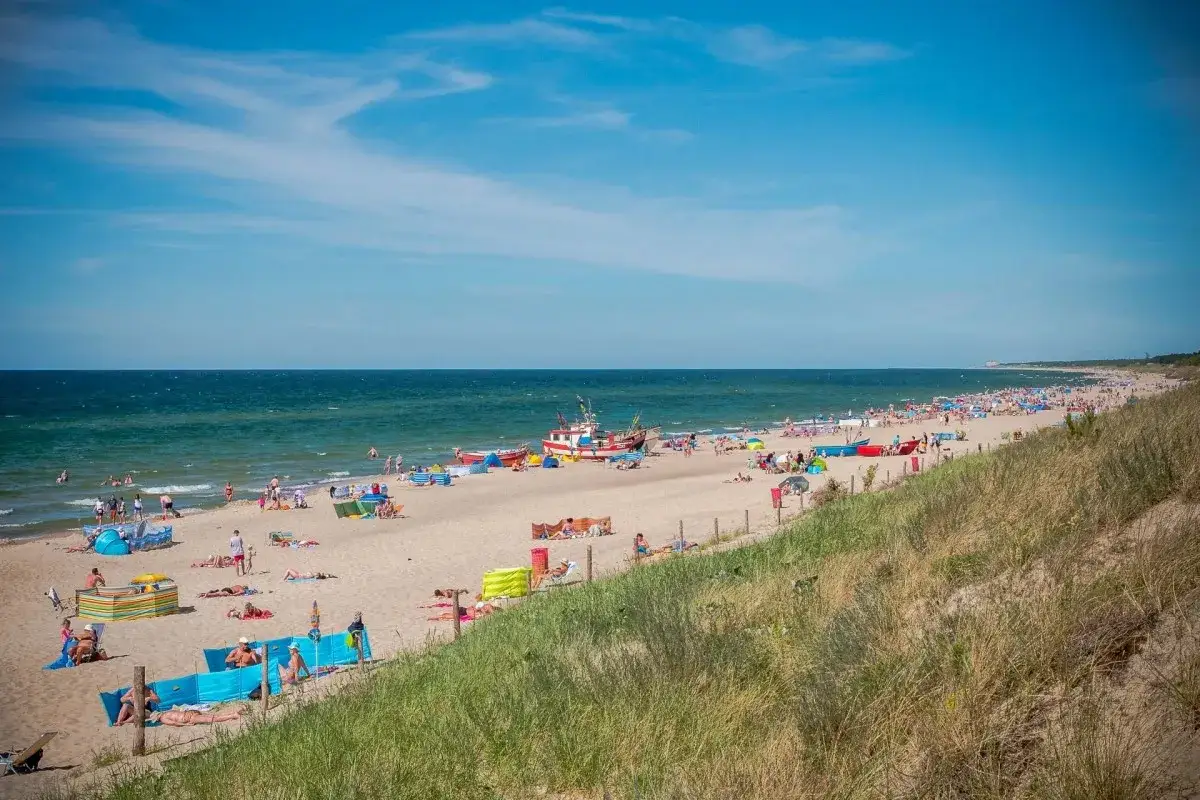 Słoneczna plaża w Dąbkach pełna turystów, kolorowe parawany i łodzie. Idealne miejsce na wakacyjne atrakcje nad morzem.
