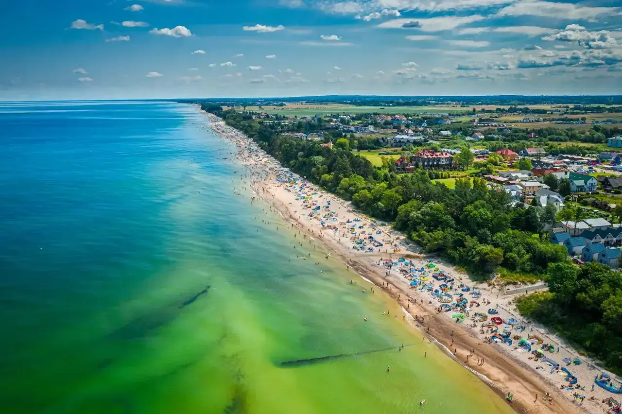 Słoneczna plaża w Mielnie pełna turystów, zielone morze i malownicze domki. Idealne miejsce na wakacyjne atrakcje.