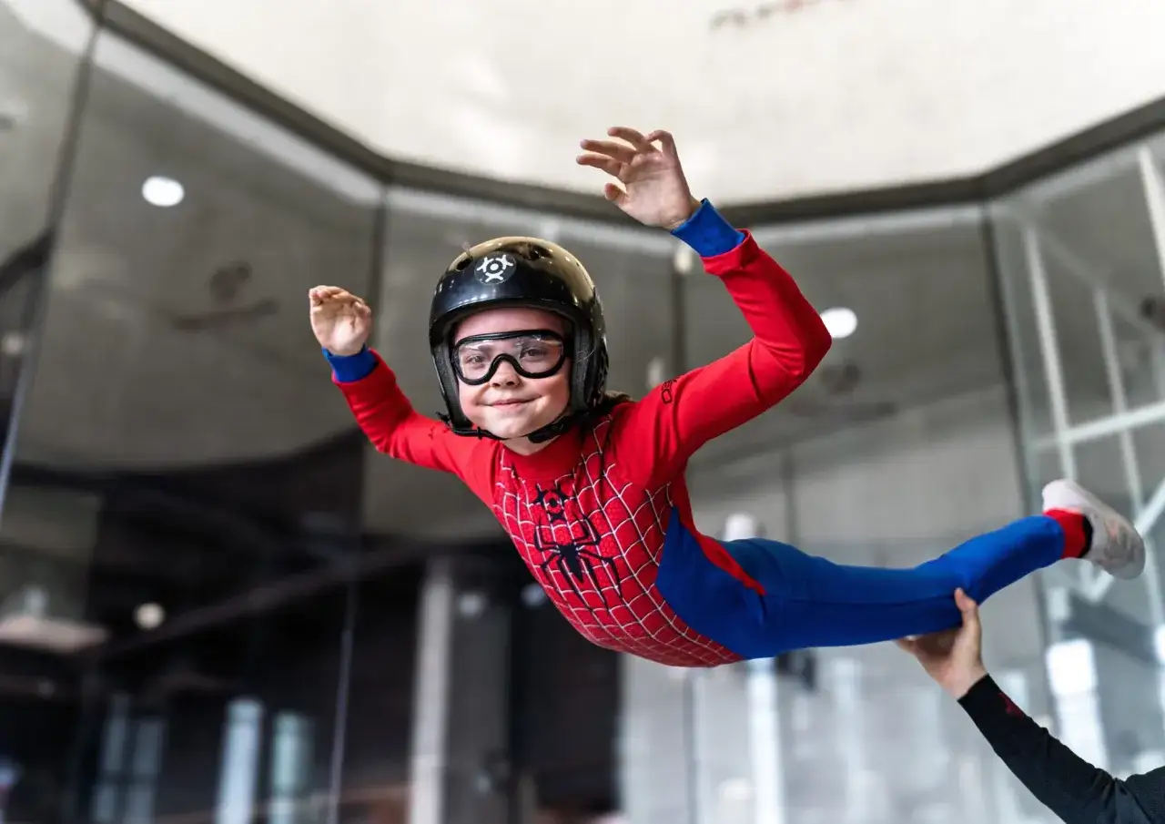Mały superbohater w stroju Spider-Mana doświadcza ekscytujących lot&oacute;w w tunelu aerodynamicznym, unosząc się w powietrzu z uśmiechem na twarzy.