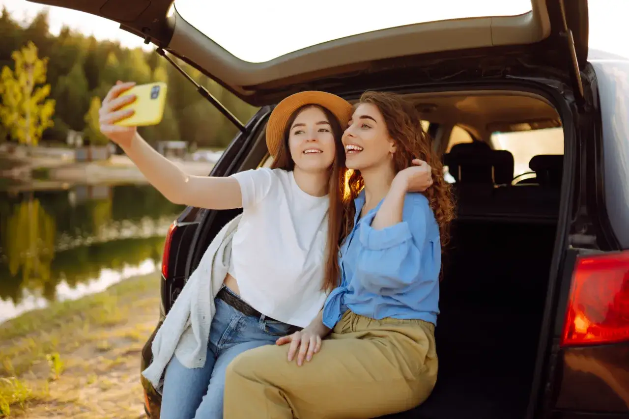 Dwie przyjaci&oacute;łki robią sobie selfie przy samochodzie nad jeziorem. Idealny weekend z przyjaci&oacute;łką!