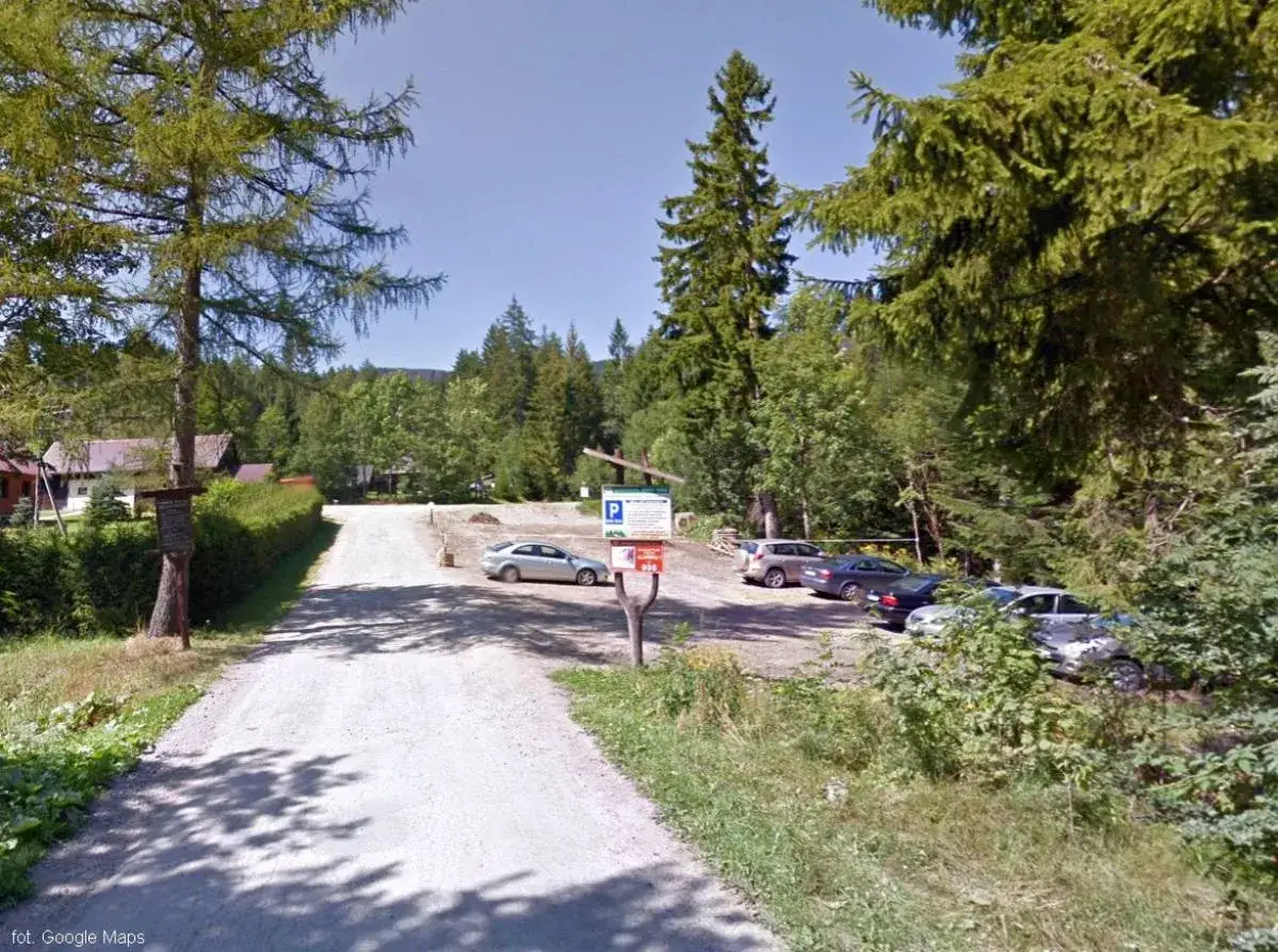 Droga do Babiej G&oacute;ry prowadzi przez parking. Kilka samochod&oacute;w zaparkowanych wśr&oacute;d drzew, gotowych na g&oacute;rską wyprawę.