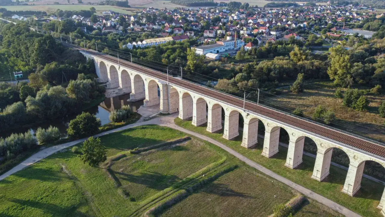 Imponujący wiadukt kolejowy nad rzeką, jedna z głównych atrakcji Bolesławca, otoczony zielenią i zabudowaniami.
