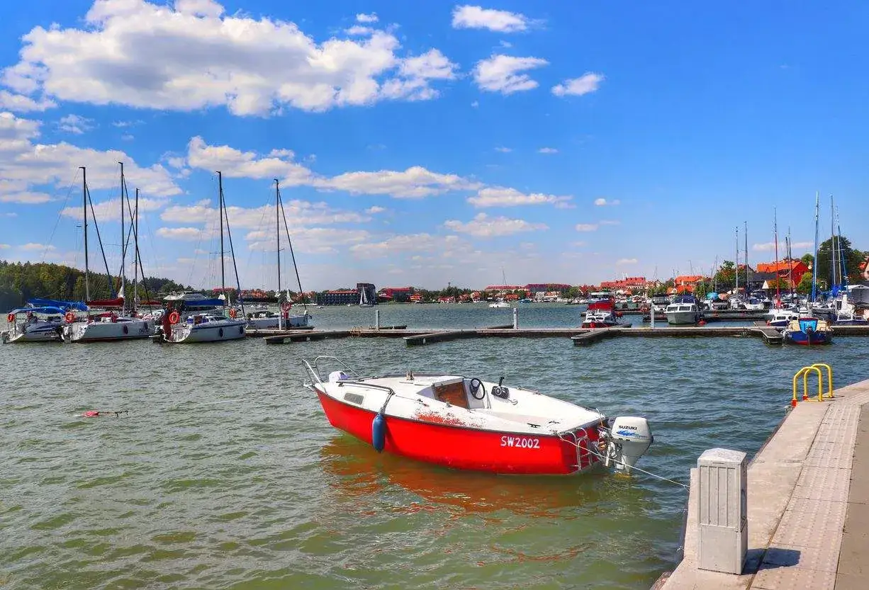 Port z żaglówkami i małą czerwoną łódką, idealne mikołajki atrakcje dla miłośników wodnych przygód.