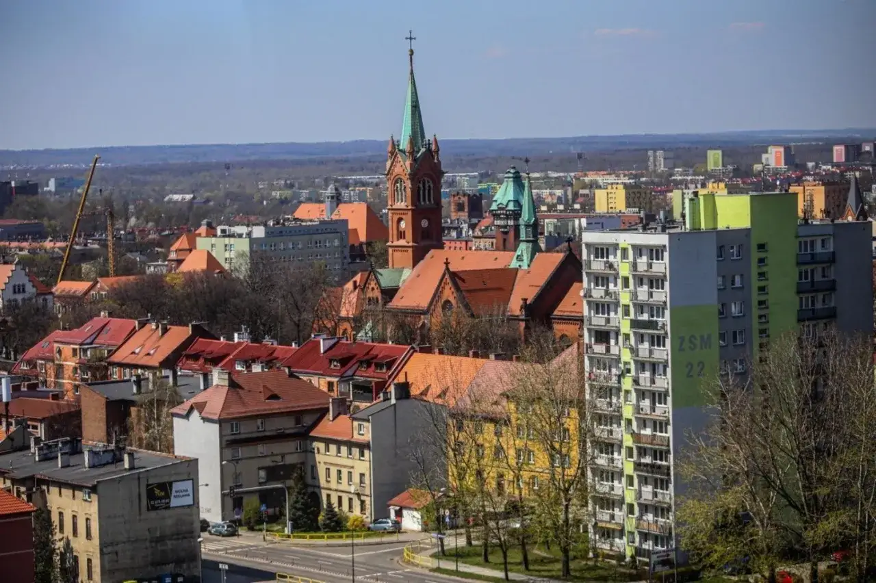 Widok na miasto z wieżą ciśnień w Zabrzu w tle. Widać kości&oacute;ł, budynki mieszkalne i drzewa.