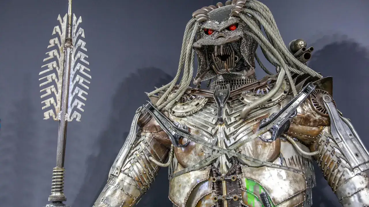 Metalowy Predator z czerwonymi oczami, zrobiony z części samochodowych, czeka na zwiedzających w Muzeum Robot&oacute;w Moszna.