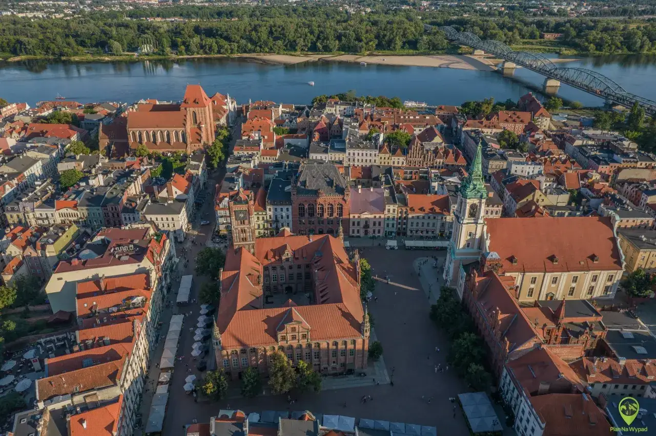 Widok z lotu ptaka na Toruń, z Wisłą i mostem w tle. Zabytkowe kamienice i kościoły tworzą malowniczy krajobraz, idealny na odkrywanie atrakcji Kujawsko-Pomorskiego.