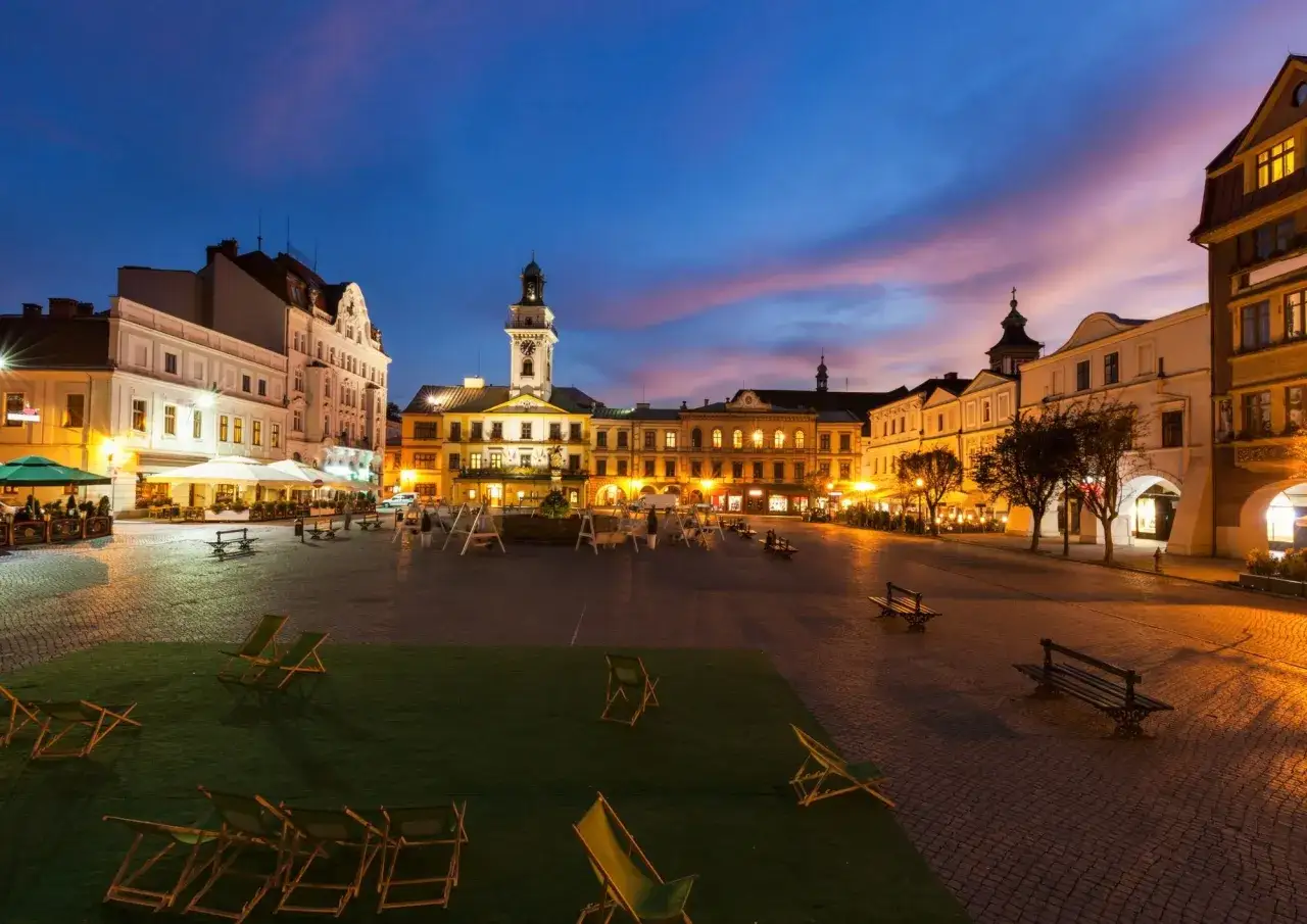 Wieczorny rynek w Cieszynie, z oświetlonymi kamienicami i wieżą ratuszową. Widać ławki, leżaki i ogródki restauracyjne. Cieszyn atrakcje zachwycają o każdej porze.