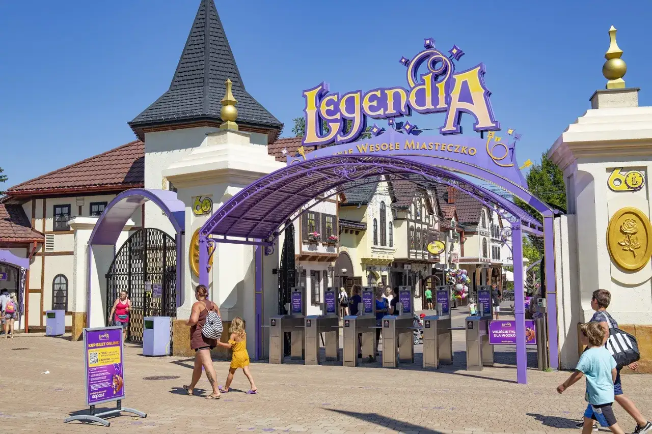 Wejście do Legendii, jednego z park&oacute;w rozrywki w Polsce. Rodziny wchodzą przez bramki, a nad nimi wisi kolorowy napis.