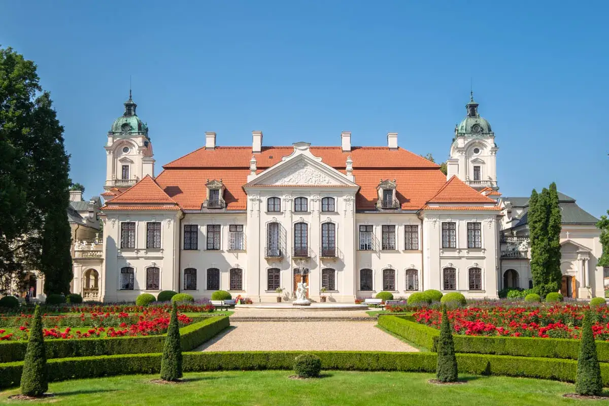 Pałac Zamoyskich z czerwonym dachem i wieżyczkami, otoczony kwitnącym ogrodem r&oacute;żanym.