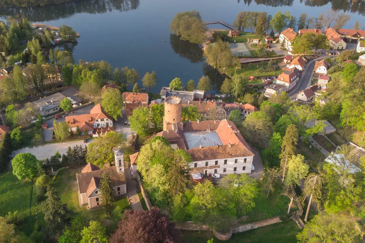 Malownicze zamki lubuskie nad jeziorem, otoczone zielenią i zabudowaniami. Widok z lotu ptaka na historyczne budowle i spokojną taflę wody.