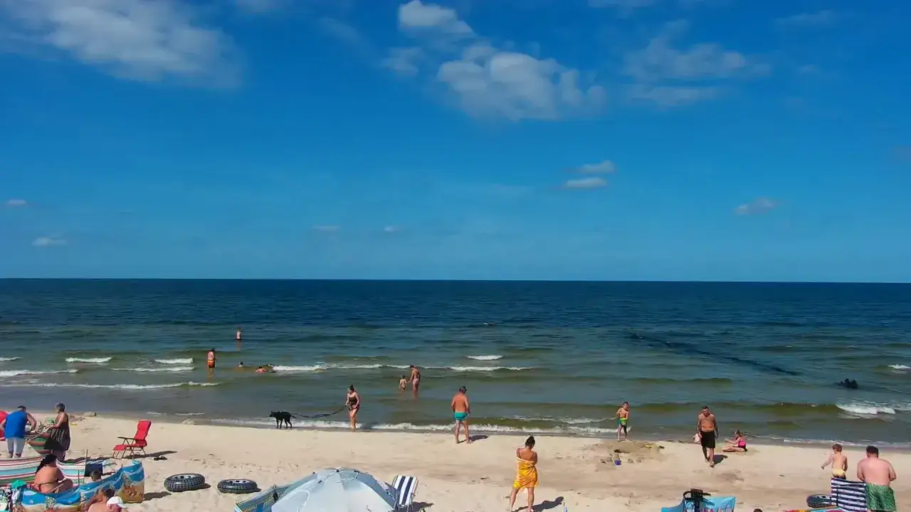 Słoneczna plaża w Mrzeżynie, ludzie kąpią się w morzu i odpoczywają na piasku. To świetne mrzeżyno atrakcje.