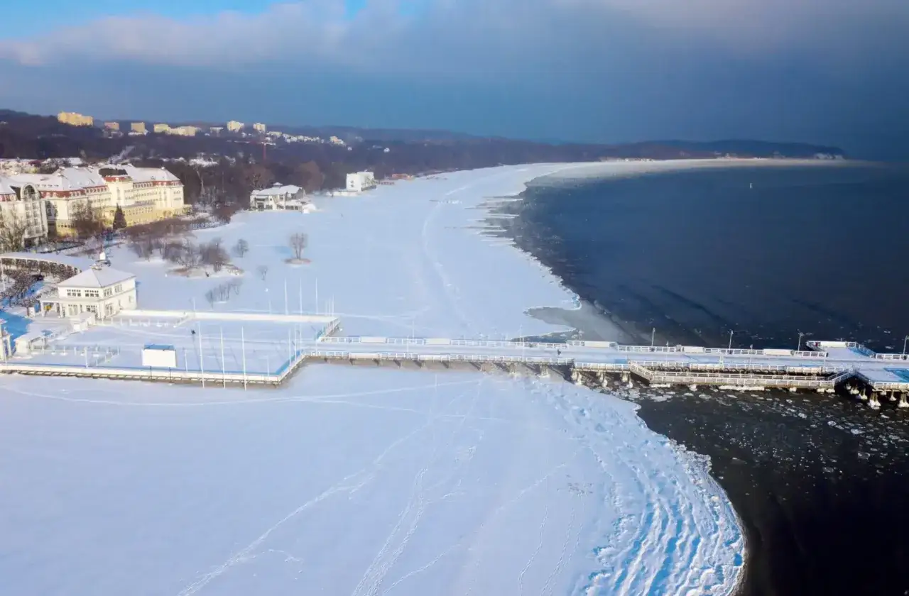 Zimowy Sopot z molo i plażą pokrytą śniegiem. Idealne miejsce, gdzie pojechać na ferie zimowe w Polsce, by poczuć morską bryzę i zimowy spok&oacute;j.