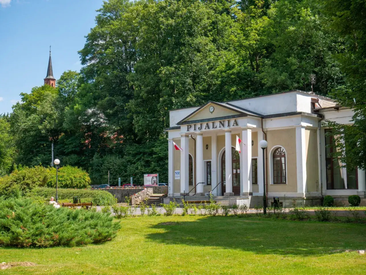 Pijalnia wód w Dusznikach Zdroju, jedna z głównych atrakcji, z kolumnowym wejściem i wieżą kościelną w tle.