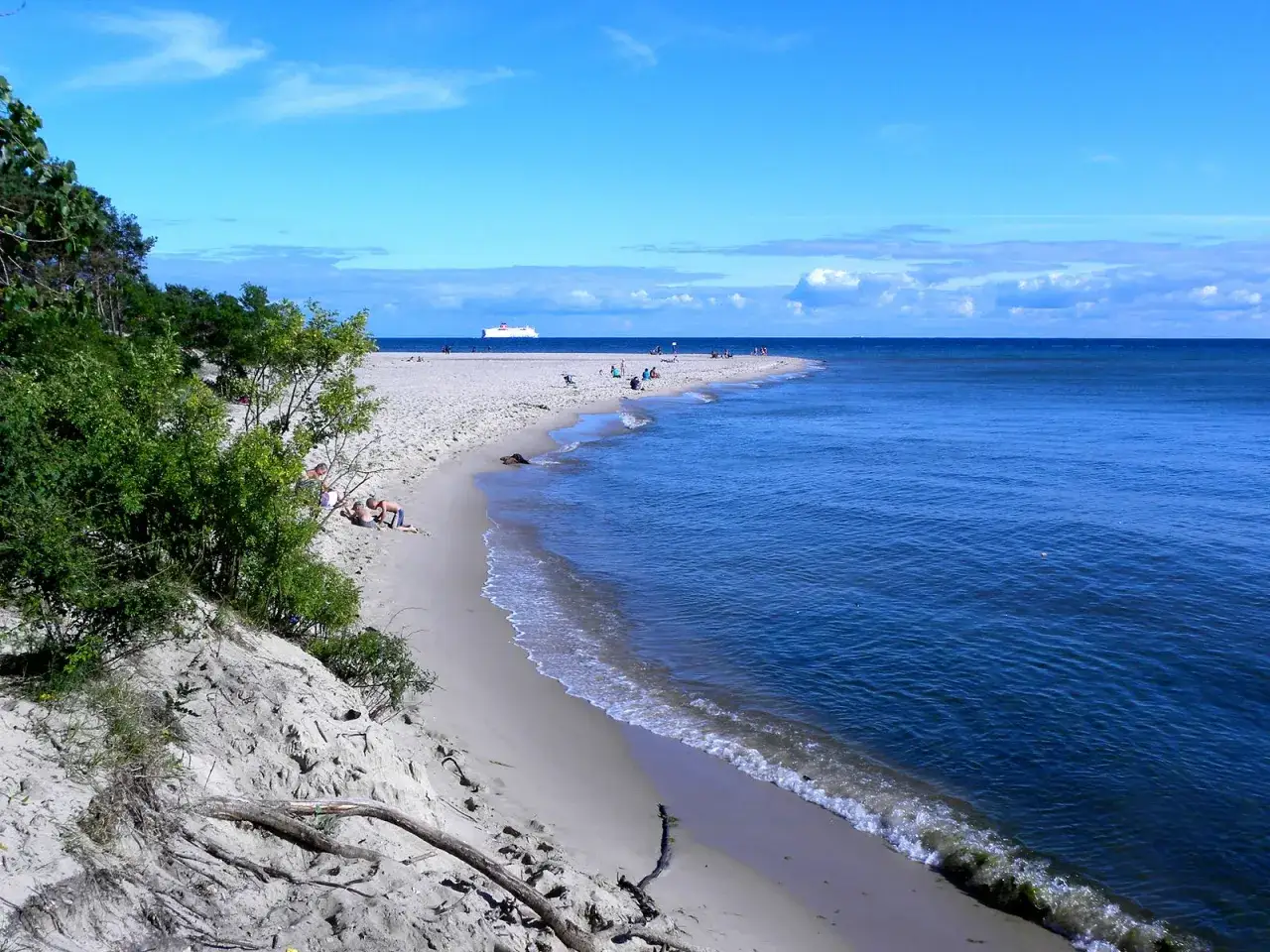 Słoneczna plaża z turkusową wodą i statkiem na horyzoncie. Idealne miejsce, gdzie najcieplej nad morzem, by odpocząć na piasku.