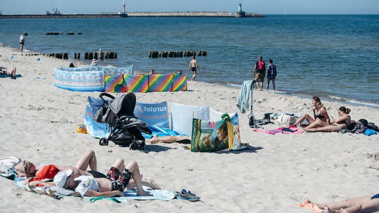 Rodzina na plaży, gdzie nad morze żeby się nie nudzić. W tle widać falochron i latarnię morską.