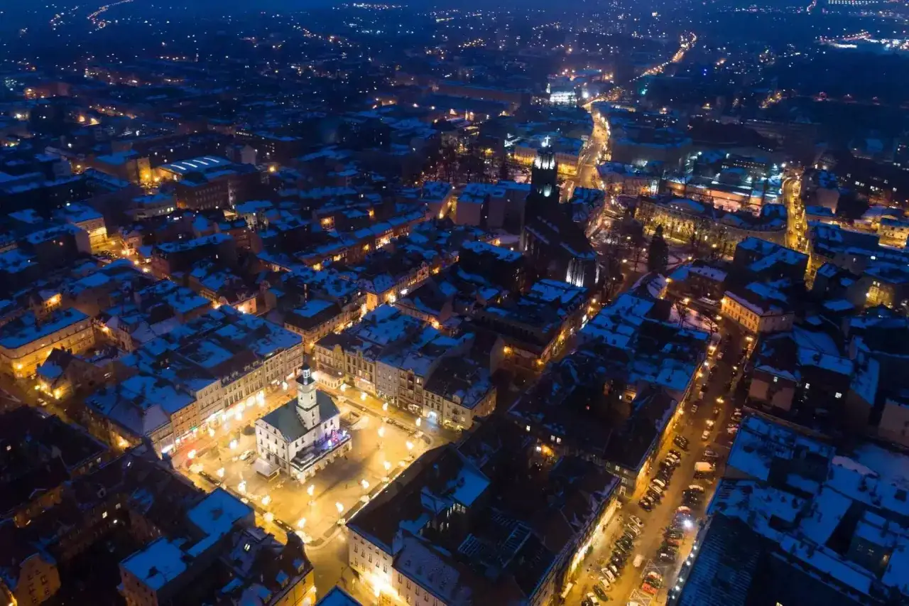 Nocny widok na Gliwice, oświetlony rynek z ratuszem i ośnieżone dachy. Miasto nocą, pełne blasku, zaprasza do odkrywania jego atrakcji.